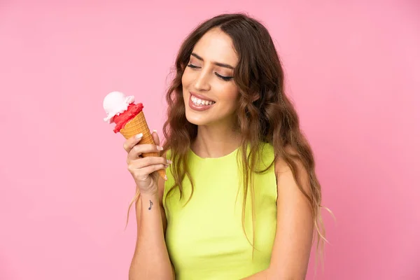 Young woman holding a cornet ice cream over isolated on a pink background