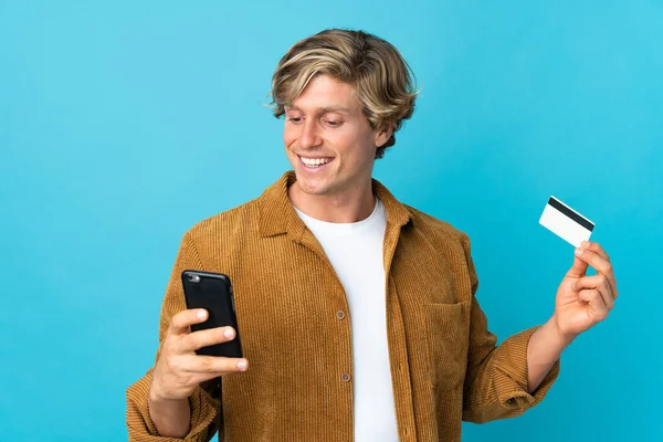 English man over isolated blue background buying with the mobile with a credit card