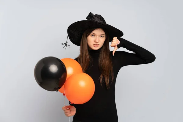 黒とオレンジの気球を持っている若い魔女は否定的な表現で親指を下に示す — ストック写真