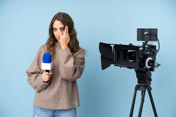 Reporter young woman holding a microphone and reporting news covering eyes and looking through fingers