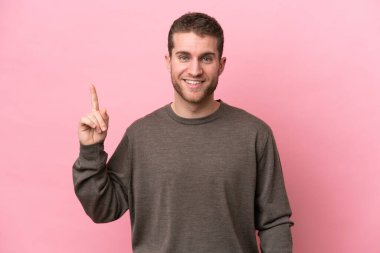 Pembe arka planda izole edilmiş genç beyaz adam harika bir fikre işaret ediyor.