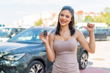 Dışarıda arabanın anahtarlarını tutan genç ve güzel bir kadın gururlu ve kendini beğenmiş.