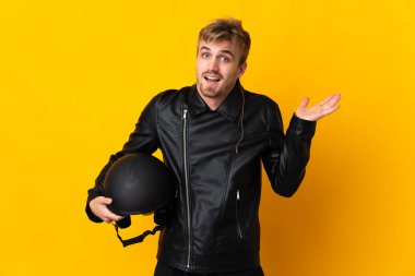 Motosiklet kasklı bir adam sarı arka planda izole edilmiş ve şok olmuş bir yüz ifadesi var.