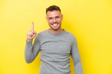 Sarı arka planda izole edilmiş beyaz, yakışıklı genç adam harika bir fikre işaret ediyor.