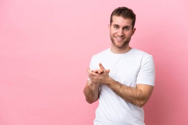 Pembe arka planda izole edilmiş genç beyaz adam alkışlıyor.