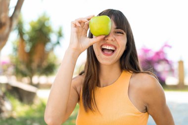 Dışarıda genç bir kadın elinde elmayla şaşkın bir ifadeyle bekliyor.