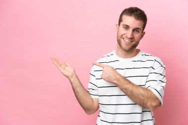 Pembe arka planda izole edilmiş genç beyaz bir adam bir ilan vermek için avucunun içinde hayali bir fotokopi makinesi tutuyor.