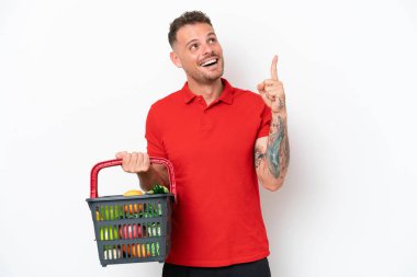 Beyaz arka planda izole edilmiş yiyecek dolu bir sepet taşıyan beyaz bir adam harika bir fikre işaret ediyor.