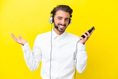 Tele pazarlamacı beyaz adam sarı arka planda izole edilmiş bir kulaklıkla çalışıyor cep telefonuyla sohbet ediyor.