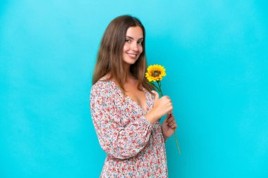 Mavi arka planda ayçiçeği tutan beyaz bir kadın gururlu ve kendini beğenmiş.