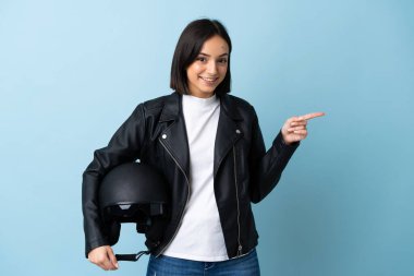 Mavi arka planda izole edilmiş motosiklet kaskı tutan kadın parmağını yana doğru gösteriyor.