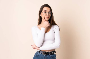 İzole edilmiş bej arka planı olan genç bir kadın yukarı bakarken bir fikir düşünüyor.