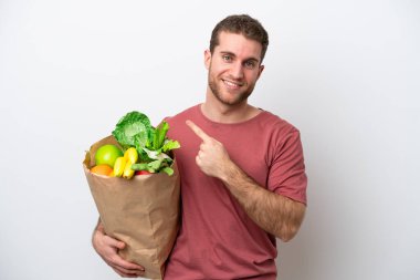 Beyaz arka planda izole edilmiş bir alışveriş torbası tutan beyaz bir adam bir ürün sunmak için kenarı işaret ediyor.