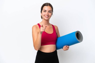 Beyaz arka planda izole edilmiş bir haldeyken yoga derslerine giden beyaz bir kadın şaşırmış ve ön tarafı işaret ediyor.