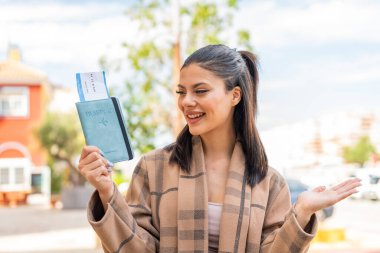 Dışarıda elinde pasaport tutan genç ve güzel bir kadın. Sürpriz bir yüz ifadesi.