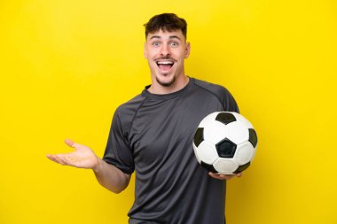 Genç futbolcu, sarı arka planda izole edilmiş, şok olmuş bir yüz ifadesi var.