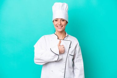 Kafkasyalı genç aşçı kadın mavi arka planda izole edilmiş bir şekilde baş parmak hareketi yapıyor.
