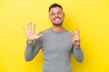 Sarı arka planda izole edilmiş beyaz, yakışıklı genç bir adam sekiz parmaklı sayıyor.