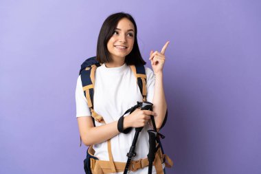 Sırt çantalı beyaz bir kadın ve mavi arka planda izole edilmiş yürüyüş direkleri harika bir fikre işaret ediyor.