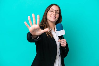 Mavi arka planda izole edilmiş genç TV sunucusu kadın parmaklarıyla beşi sayıyor.