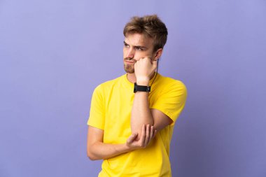 Genç yakışıklı sarışın adam, mor arka planda soyutlanmış, yorgun ve sıkılmış bir ifadeyle.