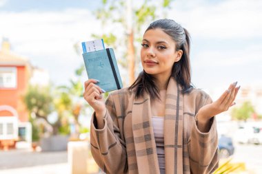 Dışarıda pasaport tutan genç ve güzel bir kadın. Omuzlarını kaldırırken şüpheyle hareket ediyor.