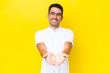 İzole edilmiş sarı arka planda genç yakışıklı bir adam. Avucunun içinde hayali bir ilan tutuyor.