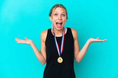 Young caucasian woman with medals isolated on blue background with shocked facial expression