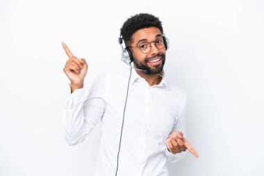 Tele pazarlamacı Brezilyalı adam beyaz arka planda izole edilmiş kulaklıkla çalışıyor. Parmak uçlarını işaret ediyor ve mutlu.
