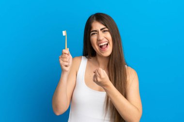 Mavi arka planda dişlerini fırçalayan beyaz bir kadın zaferi kutluyor.