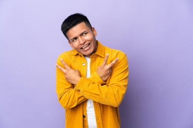 Young Ecuadorian man isolated on purple background smiling and showing victory sign