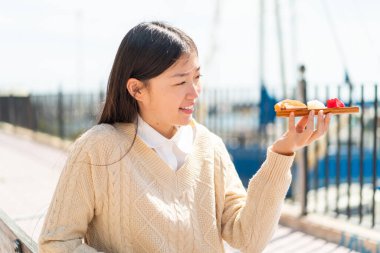 Genç Çinli kadın açık havada saşimi tutuyor, mutlu bir ifadeyle.