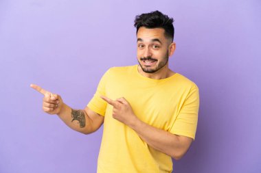 Young caucasian man isolated on purple background frightened and pointing to the side