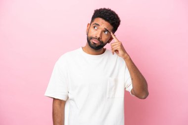 Pembe arka planda izole edilmiş genç Brezilyalı adam deliliğin hareketini yapıyor. Parmağını kafaya koyuyor.