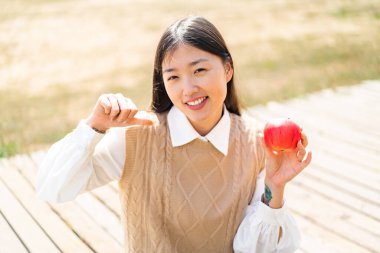 Young Chinese woman with an apple at outdoors proud and self-satisfied
