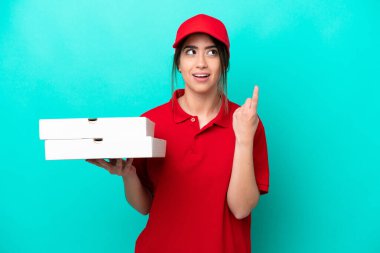 Pizza delivery woman with work uniform picking up pizza boxes isolated on blue background thinking an idea pointing the finger up