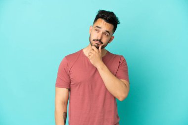 Kafkasyalı genç adam mavi arka planda izole edilmiş. Şüpheleri var.