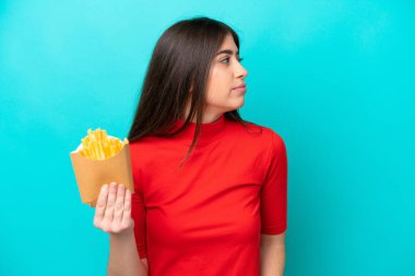Young caucasian woman catching french fries isolated on blue background looking to the side