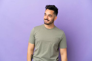 Mor arka planda izole edilmiş genç beyaz adam yana bakıyor ve gülümsüyor.