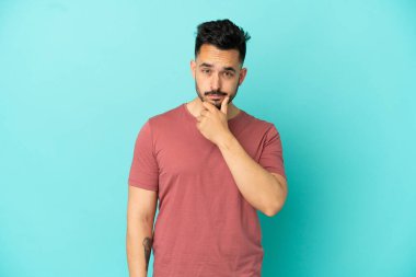 Kafkasyalı genç adam mavi arka planda izole edilmiş. Şüpheleri var.