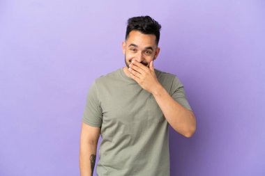 Young caucasian man isolated on purple background happy and smiling covering mouth with hand
