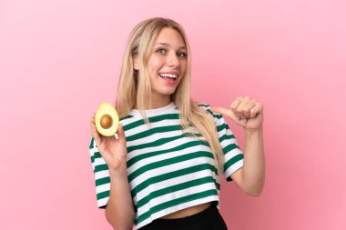 Young caucasian woman holding an avocado isolated on pink background proud and self-satisfied