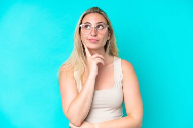 Young caucasian woman isolated on blue background With glasses and looking up