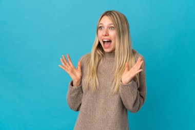 Mavi arka planda yalıtılmış genç sarışın bir kadın. Sürpriz bir yüz ifadesi var.