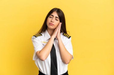 Airplane pilot isolated on yellow background making sleep gesture in dorable expression