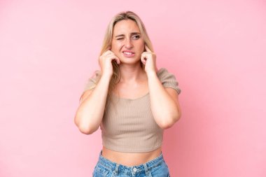 Pembe arka planda izole edilmiş genç beyaz kadın hayal kırıklığına uğramış ve kulaklarını kapatmış.