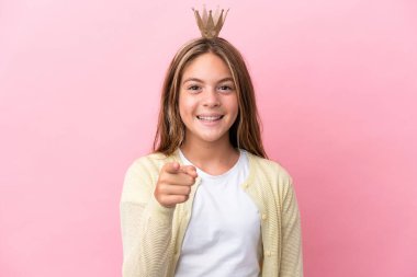 Little princess with crown isolated on pink background surprised and pointing front