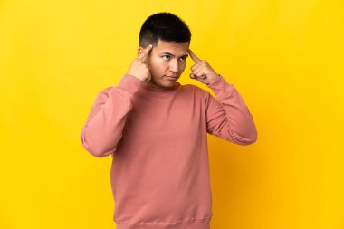 Young Ecuadorian man isolated on yellow background having doubts and thinking
