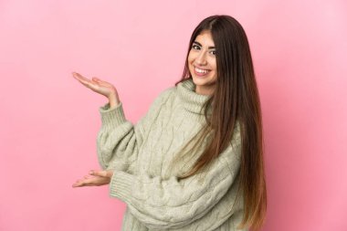 Pembe arka planda izole edilmiş genç beyaz kadın, davet edilmek için ellerini yana uzatıyor.