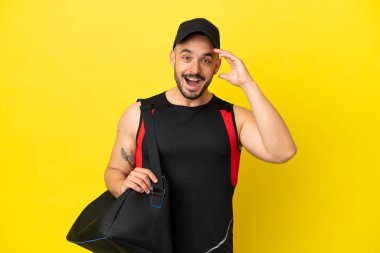 Young sport caucasian man with sport bag isolated on yellow background with surprise expression
